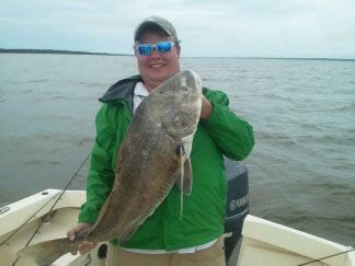 Person in green jacket holding a large fish on a boat on calm water