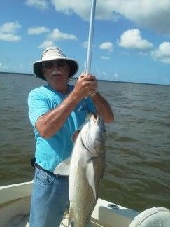 Man in blue shirt and hat holding a large fish on a boat in open water under a partly cloudy sky