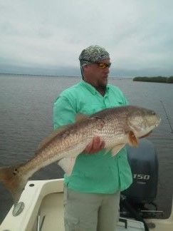 Man holding a large fish on a boat in calm water under a cloudy sky