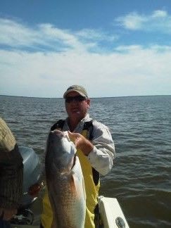Angler on a boat holding a large fish on a calm lake under a partly cloudy sky