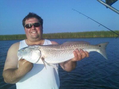 Man holding a large fish on a boat with calm blue water and marshes behind him