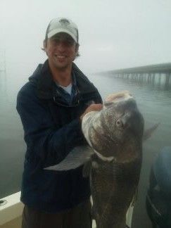 Person on a foggy pier holding a large fish beside a railing.
