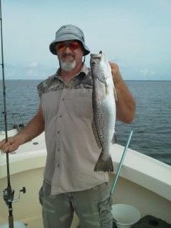 Man on a boat holding a large fish by the water, with fishing rods nearby.