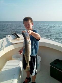 Boy on a boat holding up a large fish over the water.