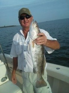 Smiling person on a boat holding a large silver fish over the water
