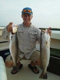 Man holding two large fish on a boat, wearing a gray shirt and blue cap.