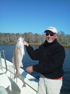 Man holding a large fish on a boat, with calm water and a blue sky behind him.