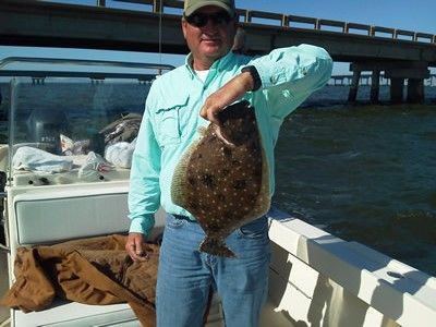 Person holding a large flat fish on a boat with a bridge in the background