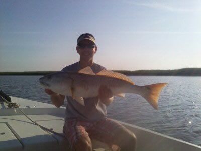 Person on a boat holding a large fish on a calm body of water at sunset