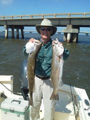 Man holding two large fish on a boat near a bridge over blue water