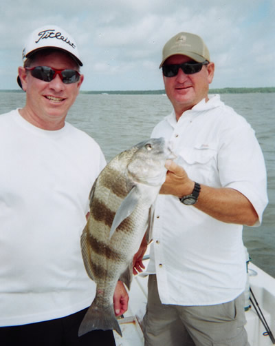 Two men on a boat holding a large striped fish on the water
