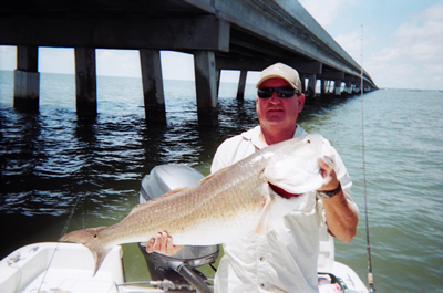 Man holding a large fish on a boat under a bridge over calm water