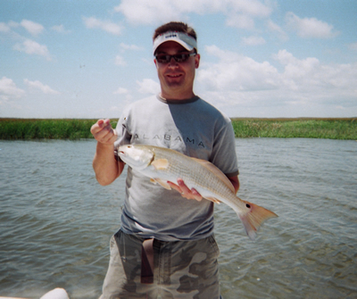 Man holding a large silver fish while standing in shallow water under a blue sky