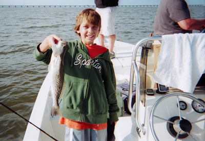 Person on a boat holding a large fish by the water