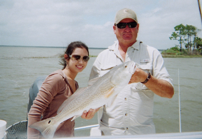 Two people on a boat holding a large fish, with water and shoreline in the background.