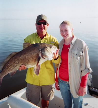 Two people on a boat holding a large fish on calm water