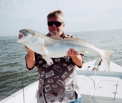 Person on a boat holding a large silver fish over the ocean.