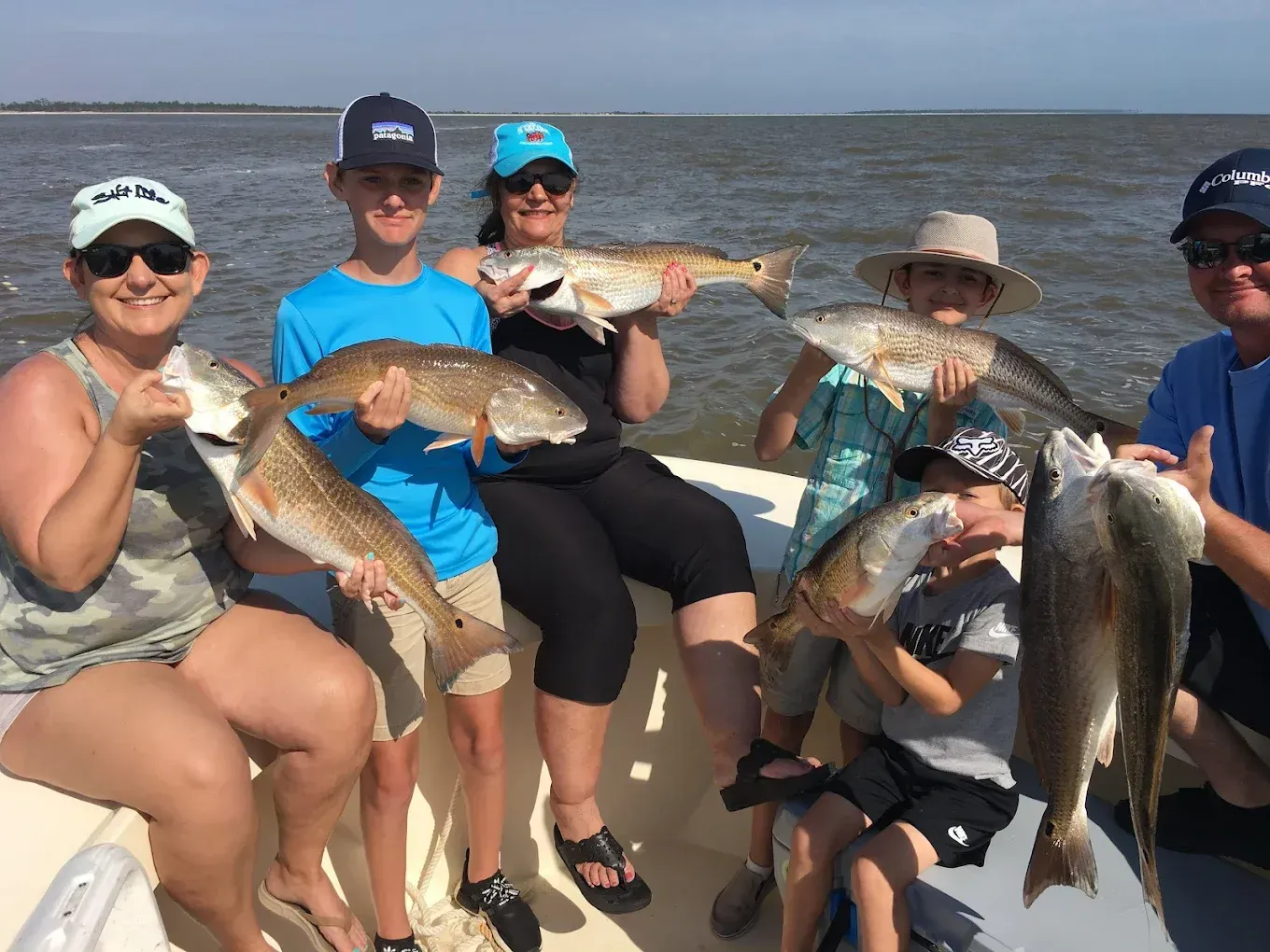 Five people on a boat holding up large fish on a sunny day at sea