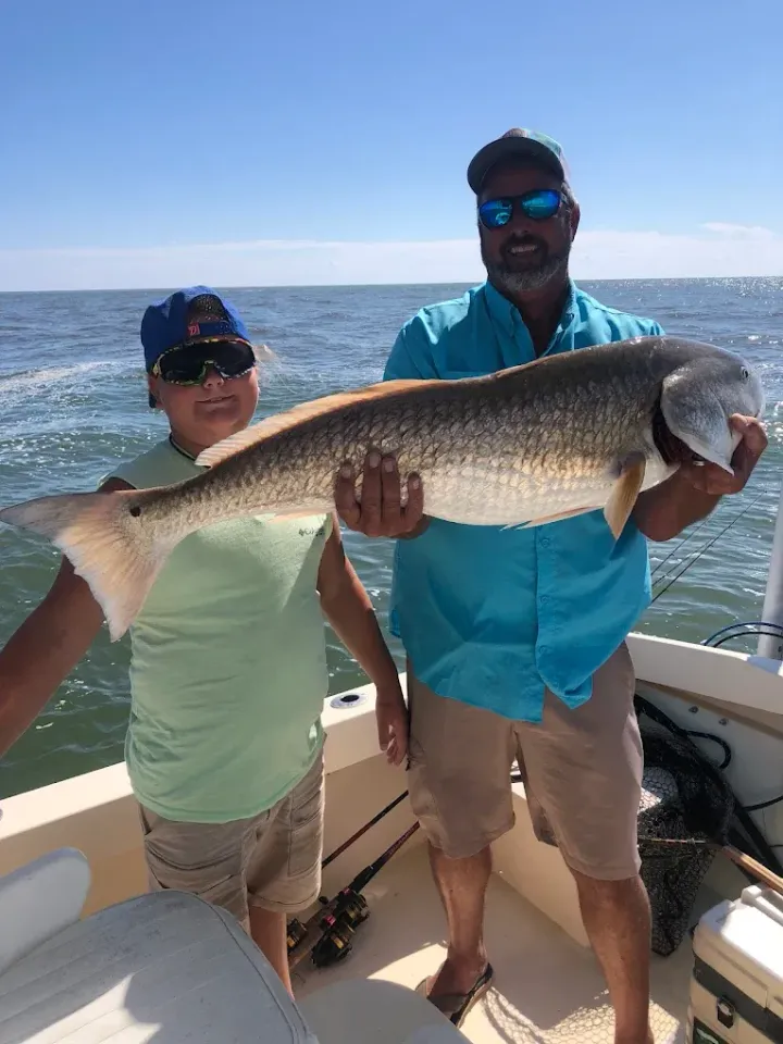 Two people on a boat hold a large fish with the ocean behind them.