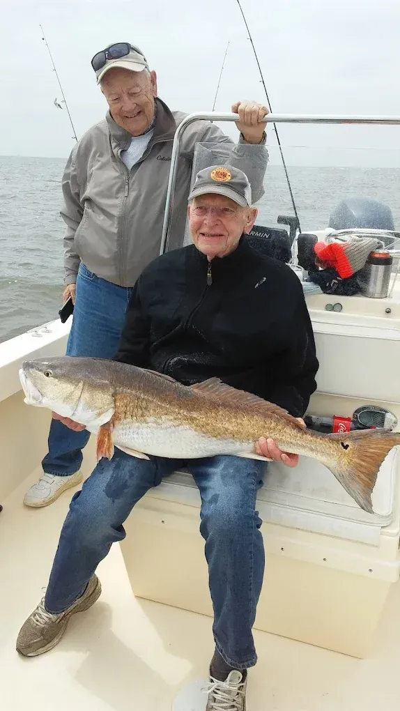 Two anglers on a boat hold a large fish on a foggy day.