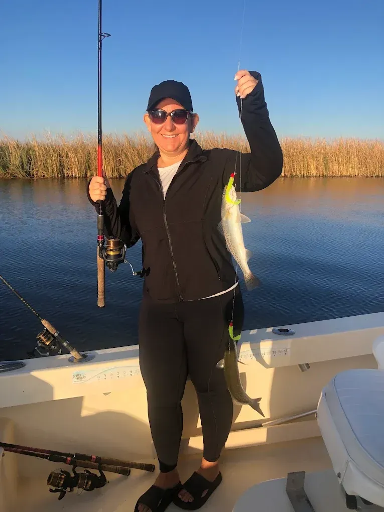Person on a boat holding a fishing rod and a caught fish at sunset on calm water.