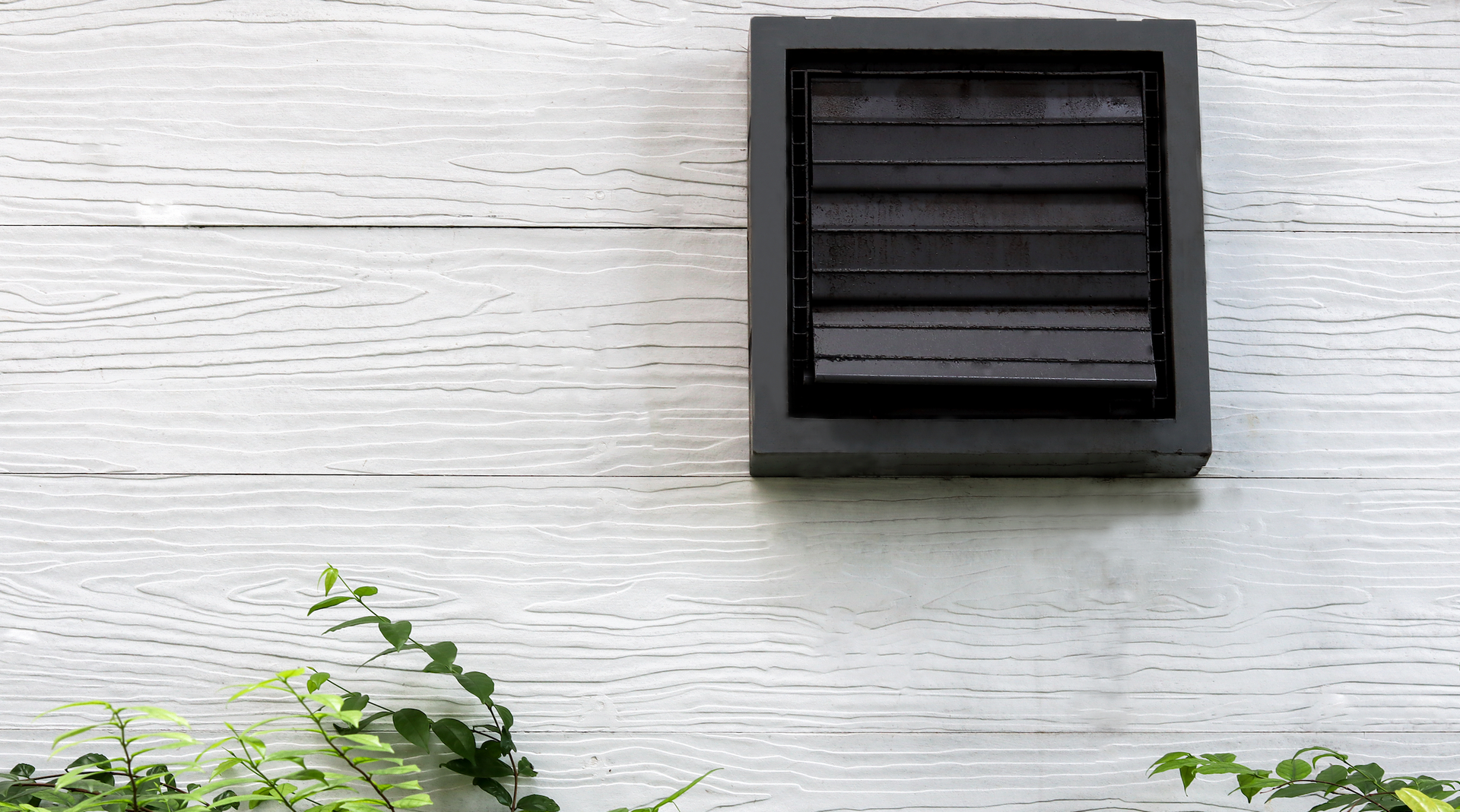 A white wall with a black vent on it.