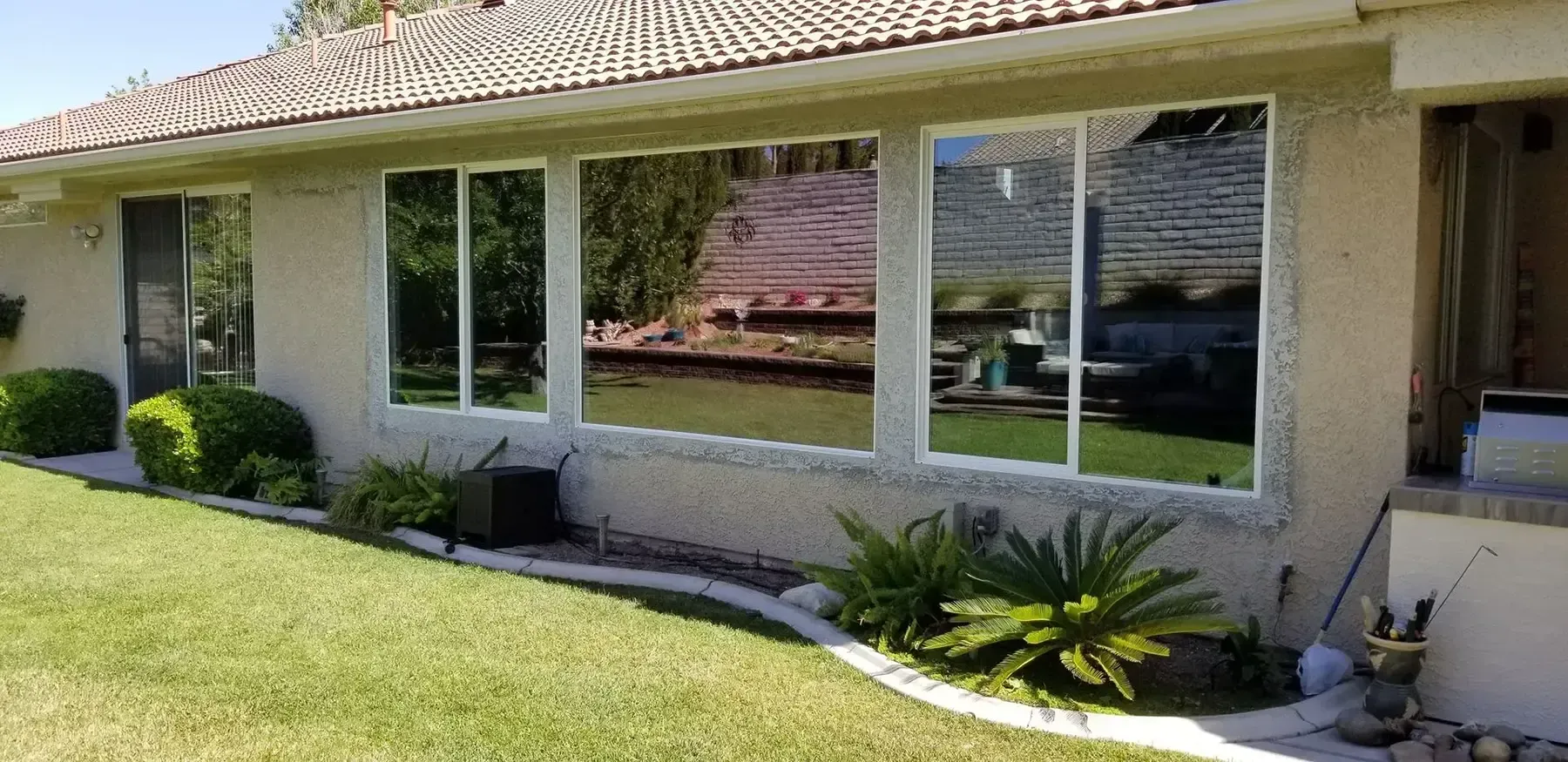 A home with large windows reflecting the outside, surrounded by greenery and lawn.