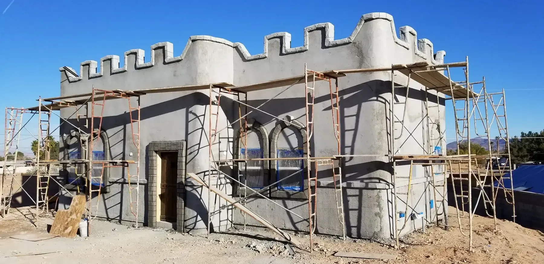 Exterior view of a castle-like building under construction with scaffolding, gray walls, and a blue sky.