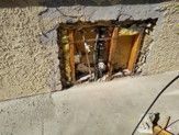 Damaged exterior wall with a rectangular hole exposing wood framing and insulation.