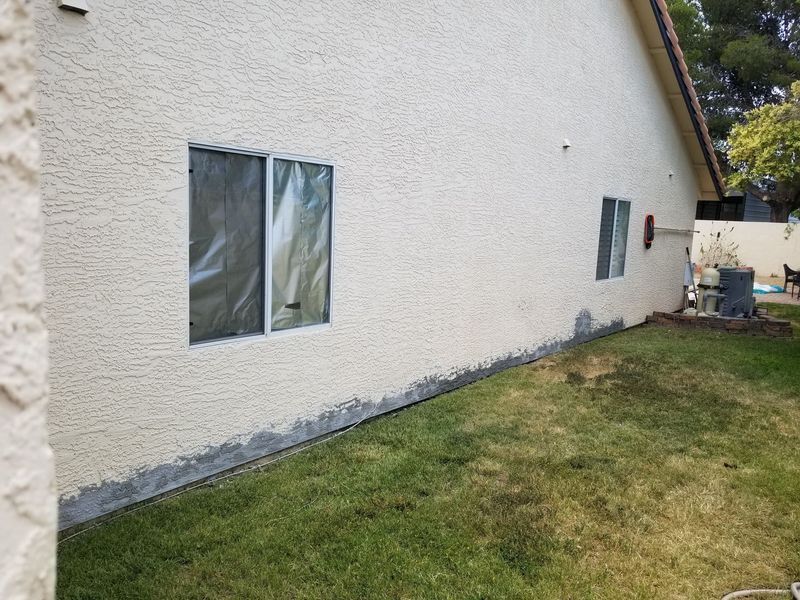 Exterior of a stucco house with two windows and a concrete base along the bottom. 