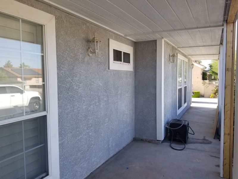 Gray stucco exterior wall with white windows and a small window, under a covered porch.