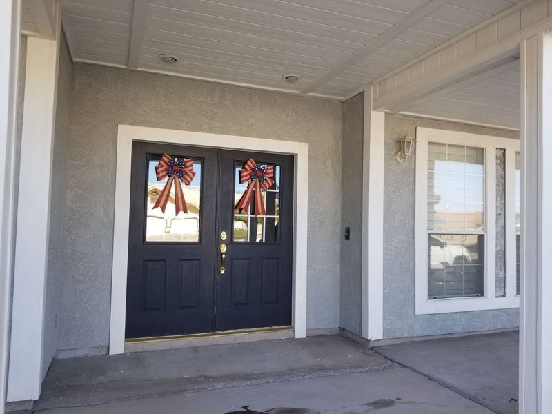 Gray stucco house entrance with black double doors, white trim, and a window.
