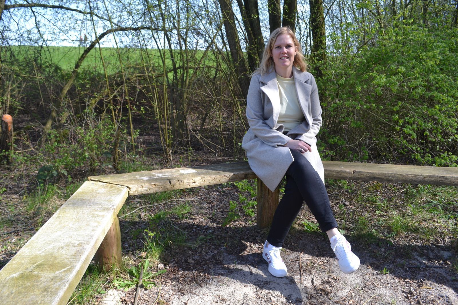 Een persoon zit op een L-vormige houten bank in een bosrijk, grasrijk buitengebied.