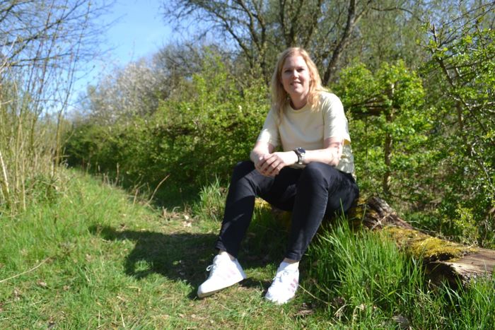 Vrouw zit op een graspad naast dichte groene struiken en bomen in zonlicht.