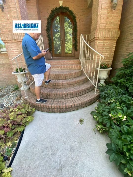 A man is standing on the steps of a house looking at his phone.