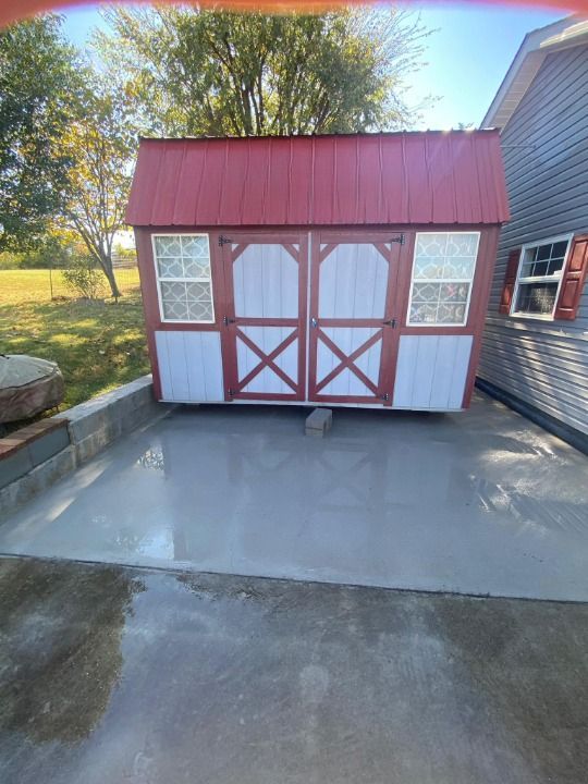 A red and white barn is sitting in a driveway next to a house.