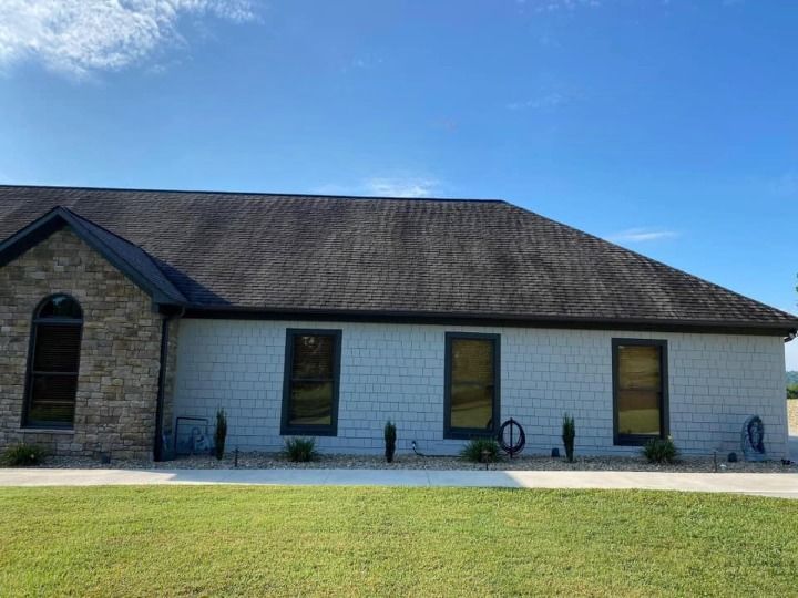 A white house with a brown roof and a lot of windows is sitting on top of a lush green field.