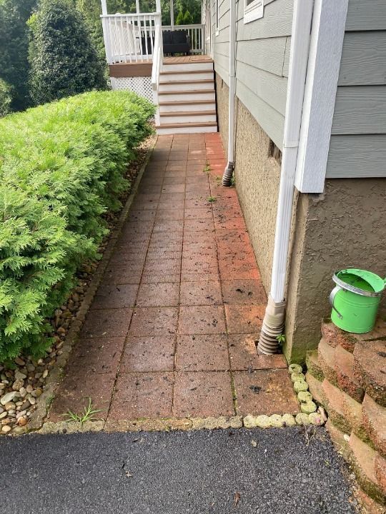 A brick walkway leading to a house with a green bucket next to it.