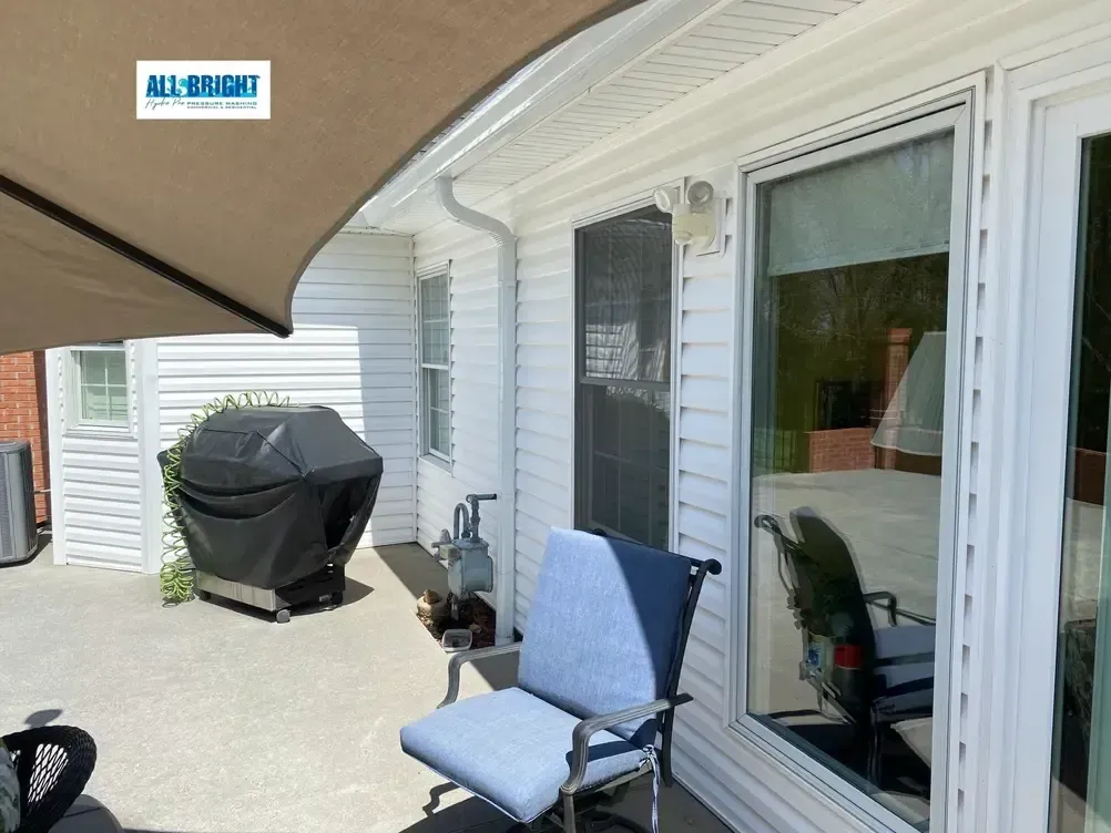 A patio with a chair and umbrella in front of a house.