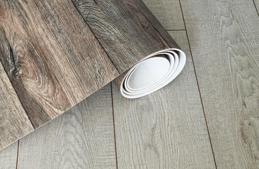 A Roll Of Wood Grain Wallpaper Is Laying On A Wooden Floor — Affordable Carpets Woolgoolga In Woolgoolga, NSW