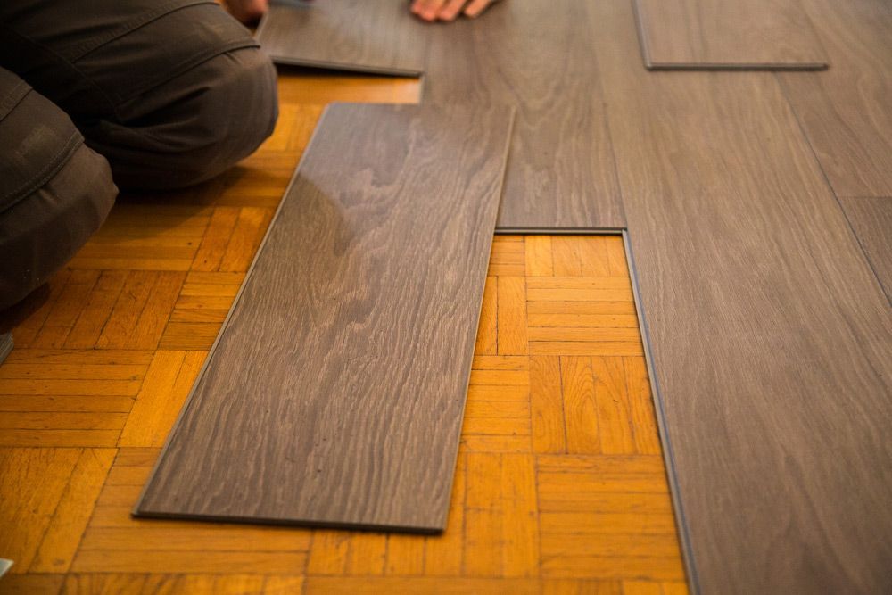 A Person Is Installing A Vinyl Plank Floor In A Room — Affordable Carpets Woolgoolga In Grafton, NSW