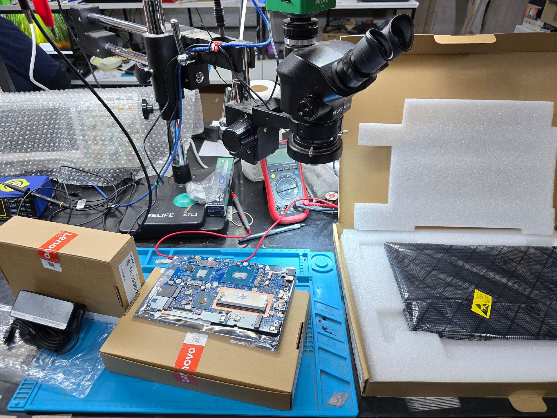 Cargador, motherboard y pantalla Lenovo originales sobre cajas en laboratorio técnico de CM Informática Bahía Blanca