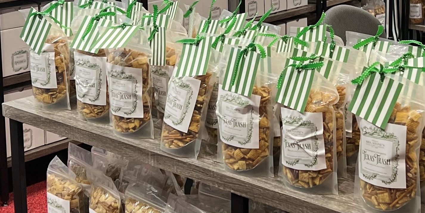 Bags of snacks on a shelf, sealed with striped green tags and ribbons. The bags have labels and are filled with a light brown treat.