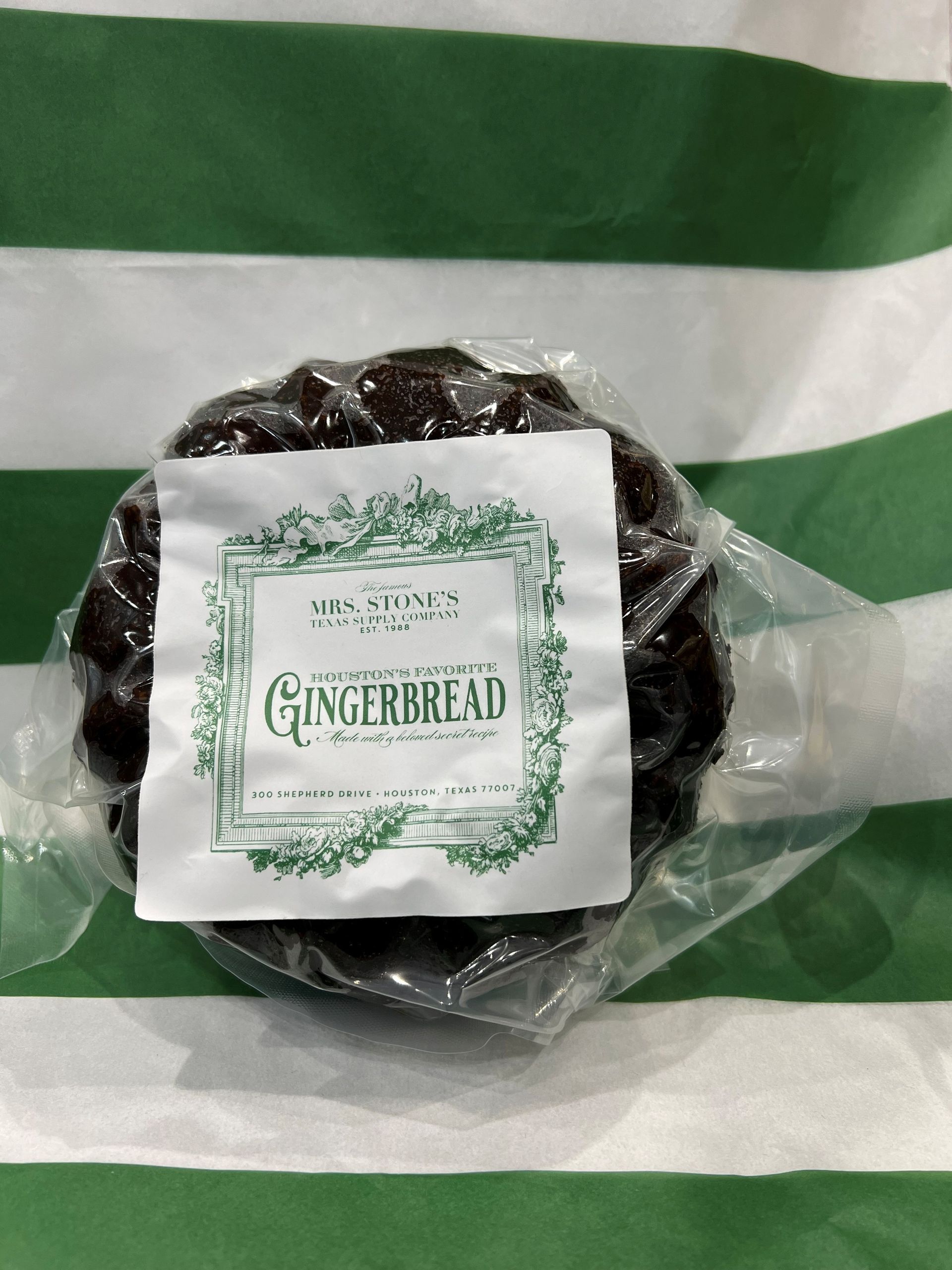 Gingerbread cookie in clear wrapper with label against green and white striped paper.