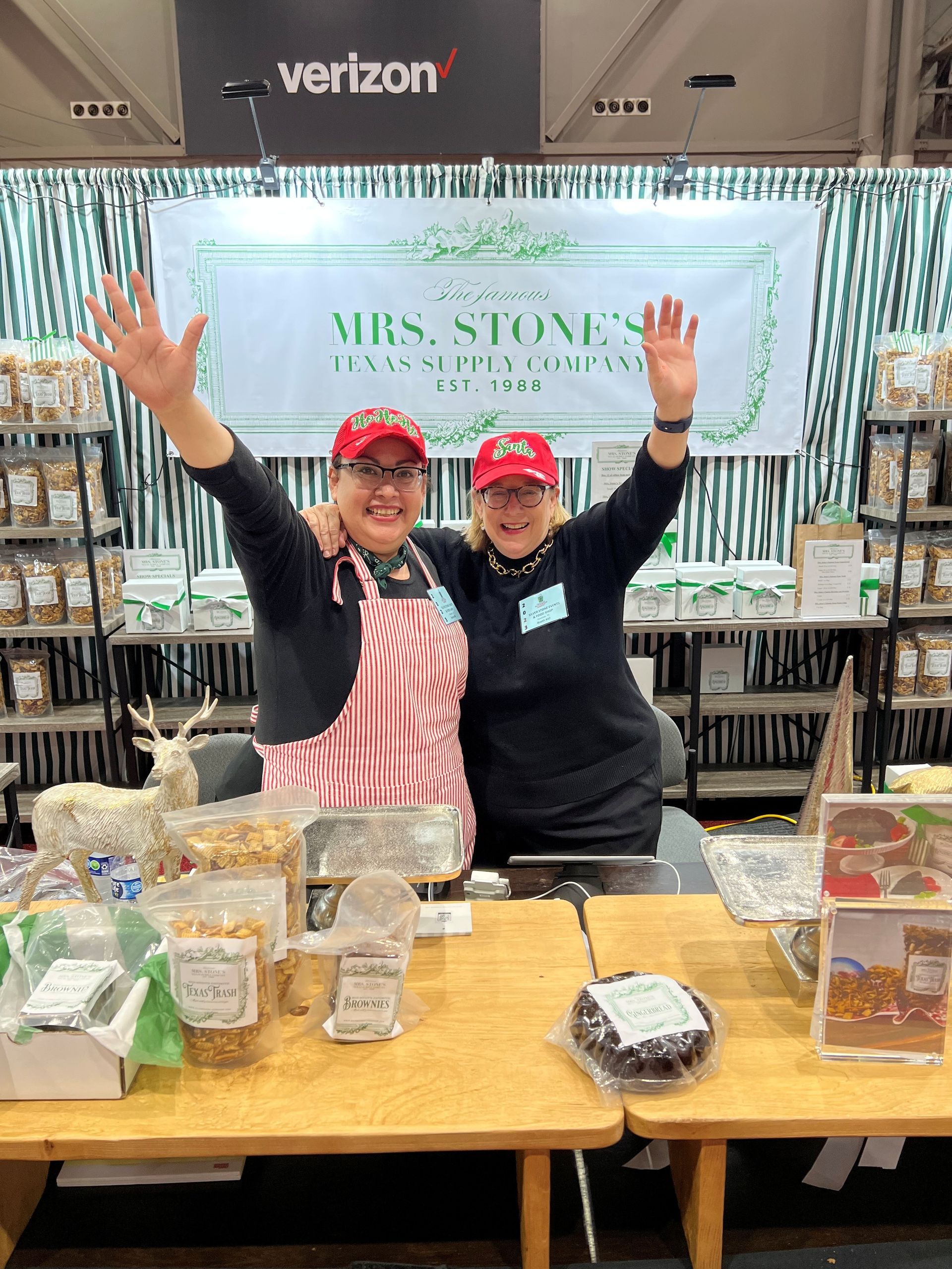 Two women behind a food vendor stand with arms raised, smiling. Mrs. Stone's sign overhead.