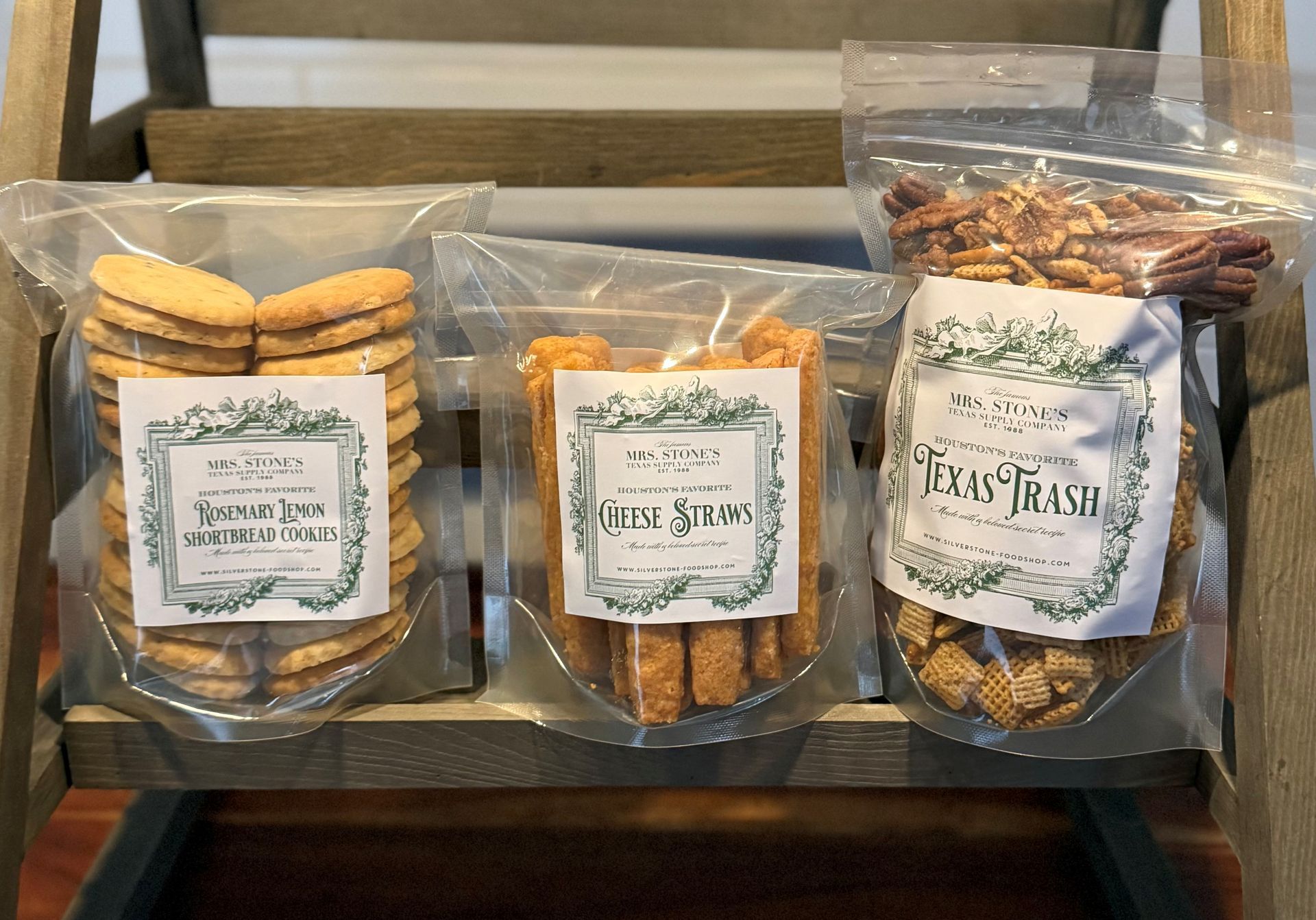 Three clear plastic bags of snacks on a wooden shelf: cookies, shortbread, and