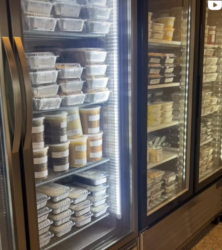 Refrigerated display case filled with prepared food containers and jars; lit by vertical LED lights.
