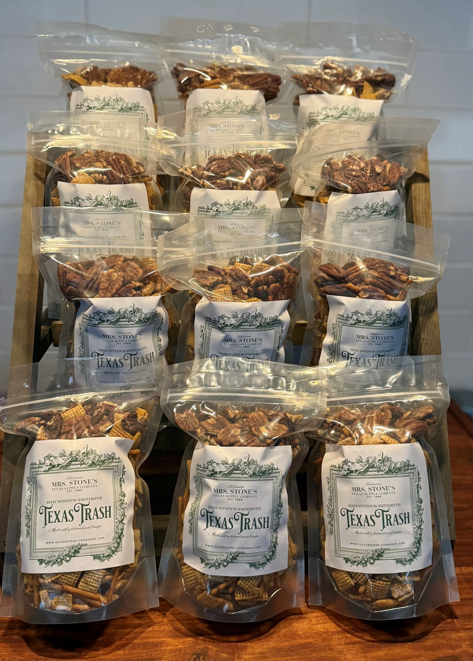 Bags of various baked goods displayed on a wooden stand against a white brick wall.