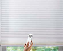 a person is holding a remote control in front of a window cellular shade blind .
