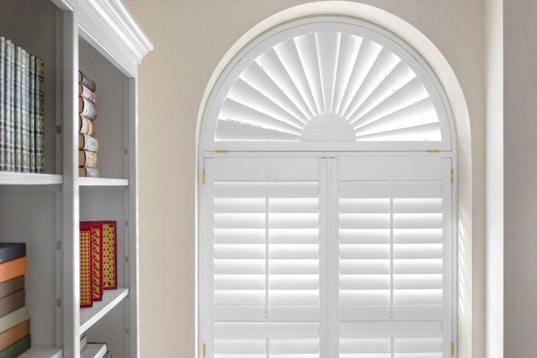 A room with a bookshelf and a window with shutters on it.